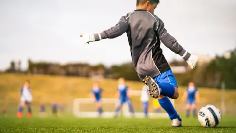 Un enfant en uniforme se prépare à frapper le ballon.