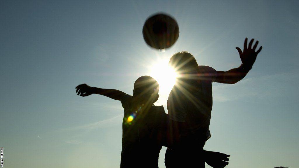 A silhouette of two players heading a football