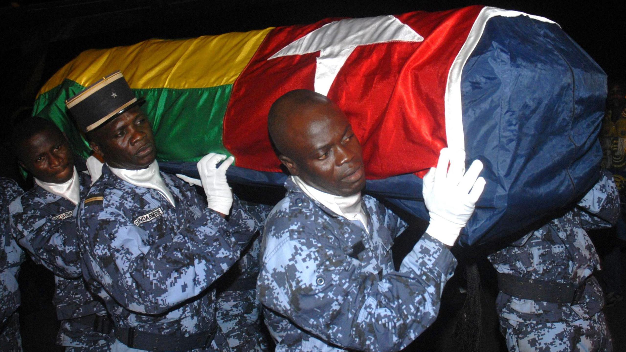 Four gendarmes portant un cercueil portant le drapeau togolais.