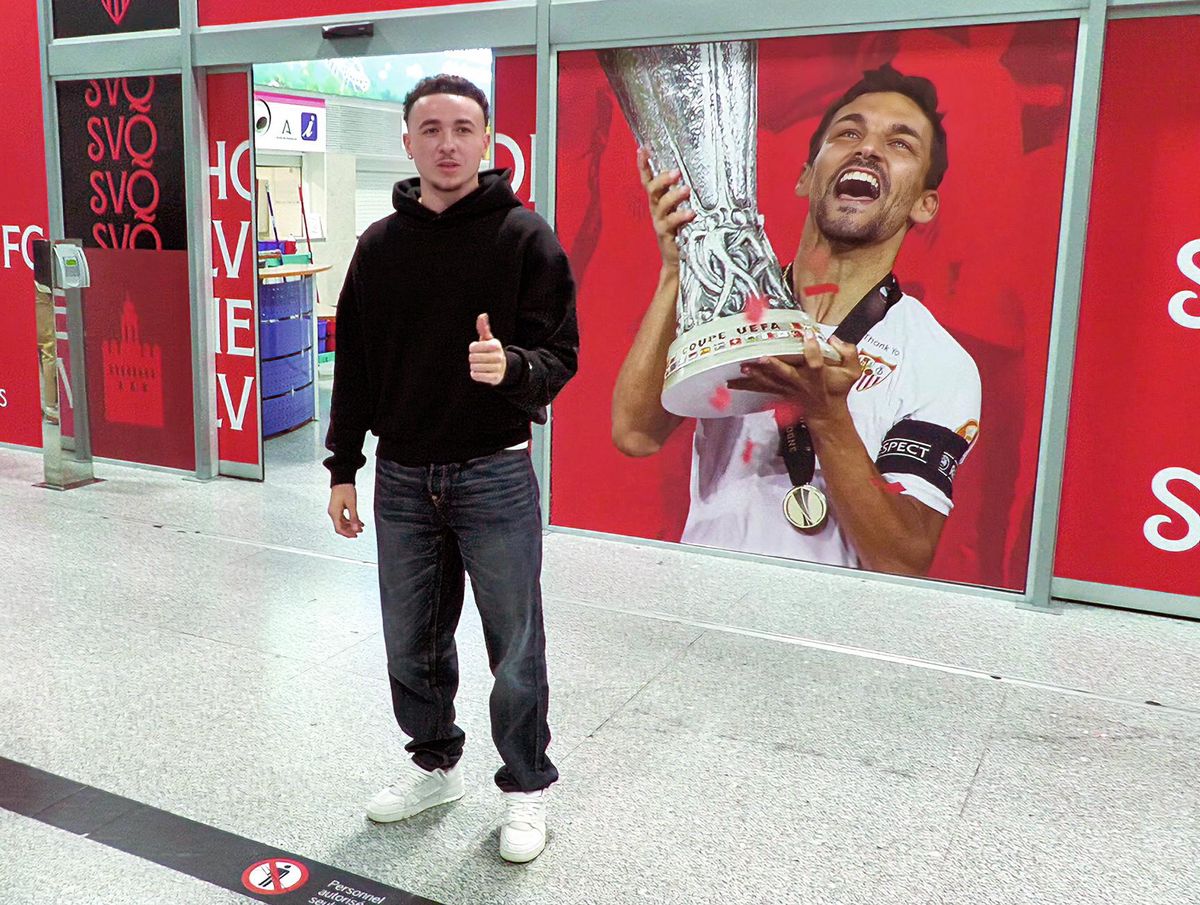 Le joueur de football suisse Ruben Vargas à l’aéroport de Séville, levant le pouce devant un panneau de Séville FC.