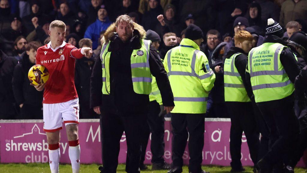 Police et stewards font une barrière devant les fans alors que James McClean de Wrexham effectue une touche.