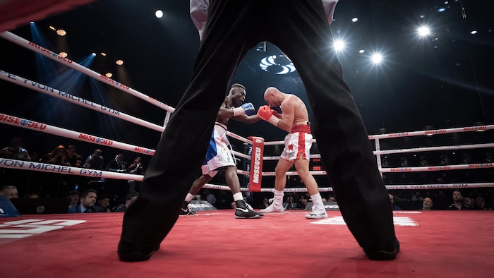 Deux boxeurs s'affrontent avec, en avant-plan, les jambes de l'arbitre.